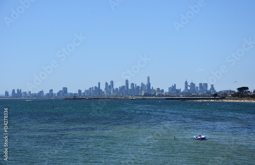 Melbourne skyline from Brighton Beach Gardens (Victoria Australia). View over the city of Melbourne in the Port Phillip Bay and colourful bathing boxes on the beach. © katacarix