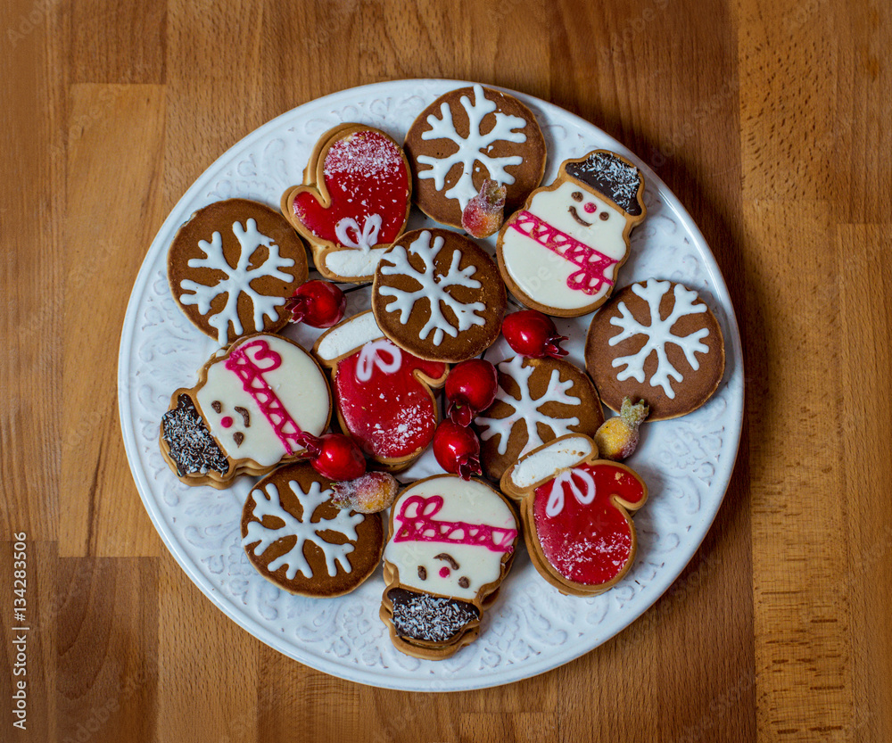 Christmas or Valentine decorated cookies on white plate. Gingerbread cookies on vintage wooden background. Chocolate biscuits in New Year, winter holidays style over wooden background. Top view