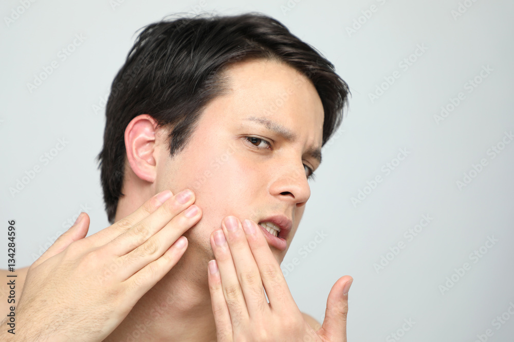 Young man checking his skin, men's skincare concept, acne treatment Young man checking his skin, men's skincare concept, acne treatment