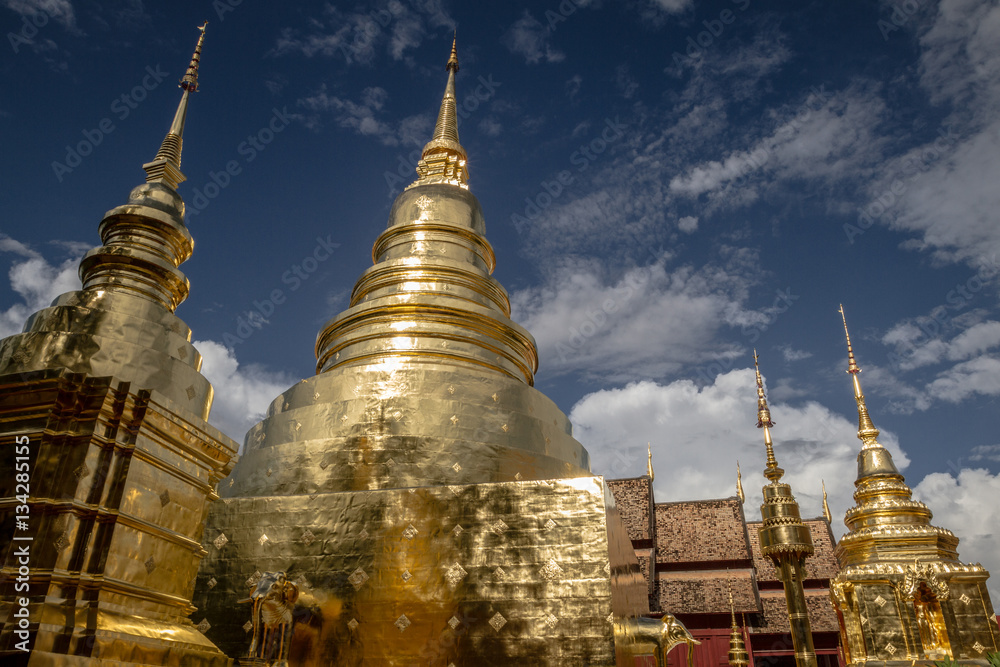 Fototapeta premium Low angle view of gold pagoda with golden chedi at Wat Phra Singh temple in Chiang Mai, Thailand, with amazing cloudy sky background