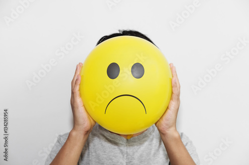 A man holding a yellow balloon with sadly face emoticon instead of head