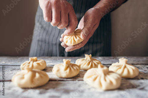 Man making khinkali for his family close-up. Unrecognizable cook preparing georgian traditional meal of dough and meat at kitchen. National cuisine, cooking process concept