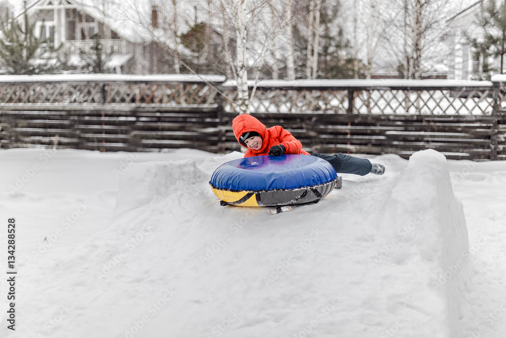 Boy with the inflatable sledge, snow tube, inner tube, lies on snow