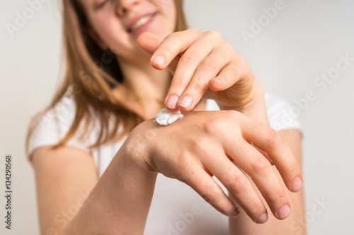 Smiling young woman applying cream on her hands