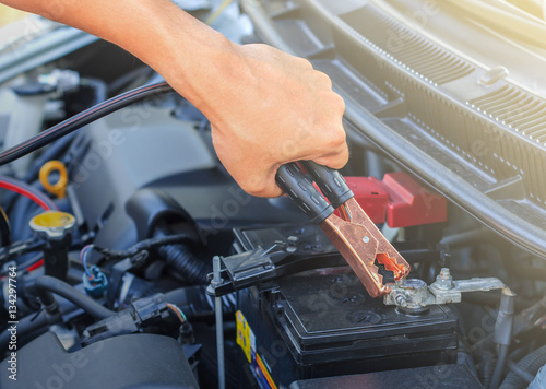 A car mechanic uses battery jumper cables to charge a dead batte