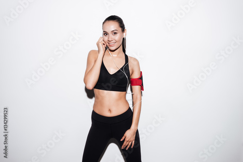 Happy fitness woman with armband standing and listening to music