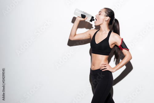 Beautiful young fitness woman standing and drinking water