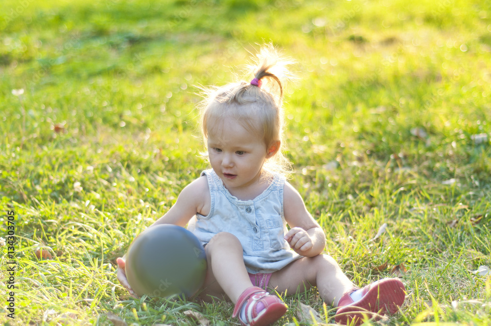 Cheerful little girl playing with a ball in a summer park on the Cheerful little girl playing with a ball in a summer park on the