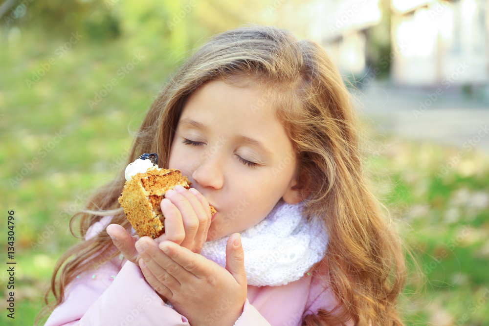 Cute little girl eating tasty cake outdoors, close up view