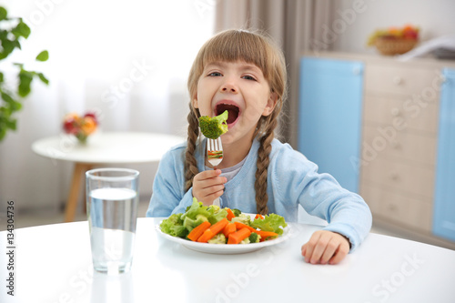 Small girl eating vegetables in kitchen