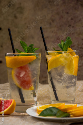 Two glass cups of water with red orange, lemon, mint and ice. Fr