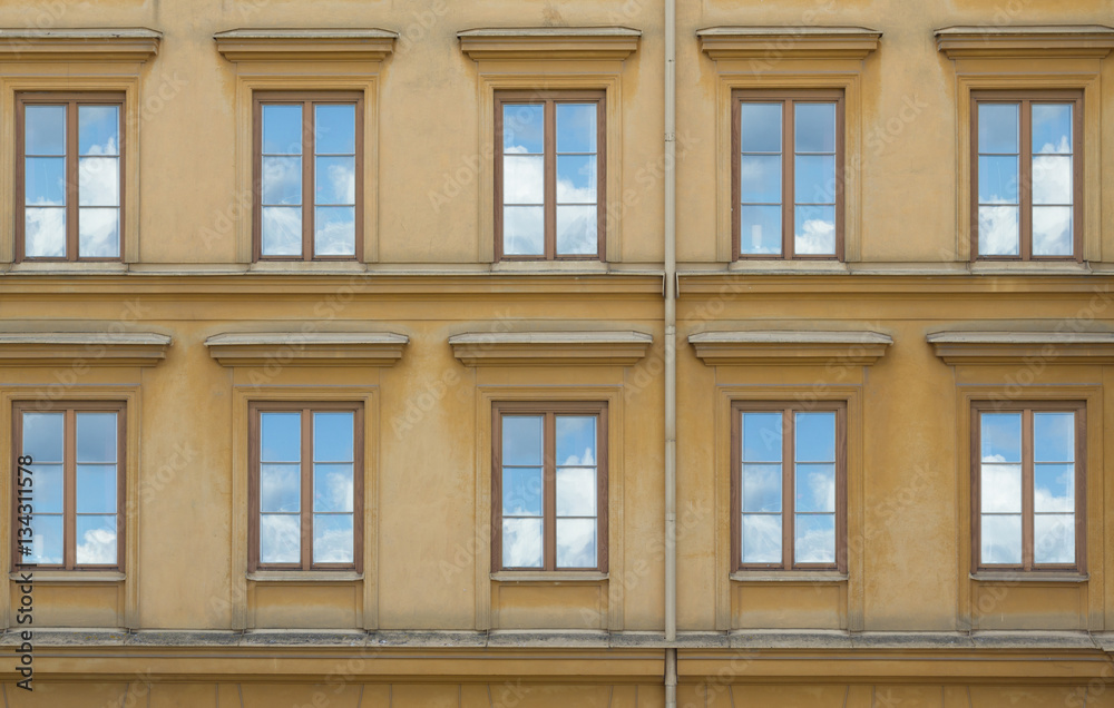 old yellow building with windows reflection of clouds in them