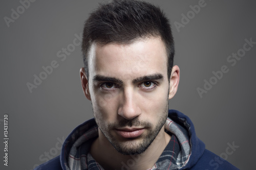 Close up portrait of angry young bearded male wearing hoodie staring at camera