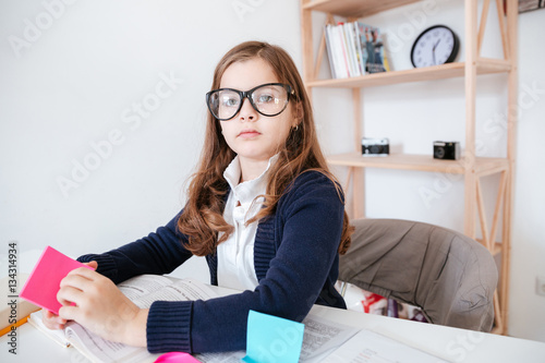 Little girl in glasses reading book and using stick notes photo