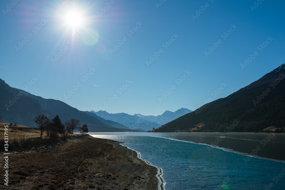 Fototapeta premium Sonniger Wintertag im Dezember am Reschensee in Südtirol / Italien