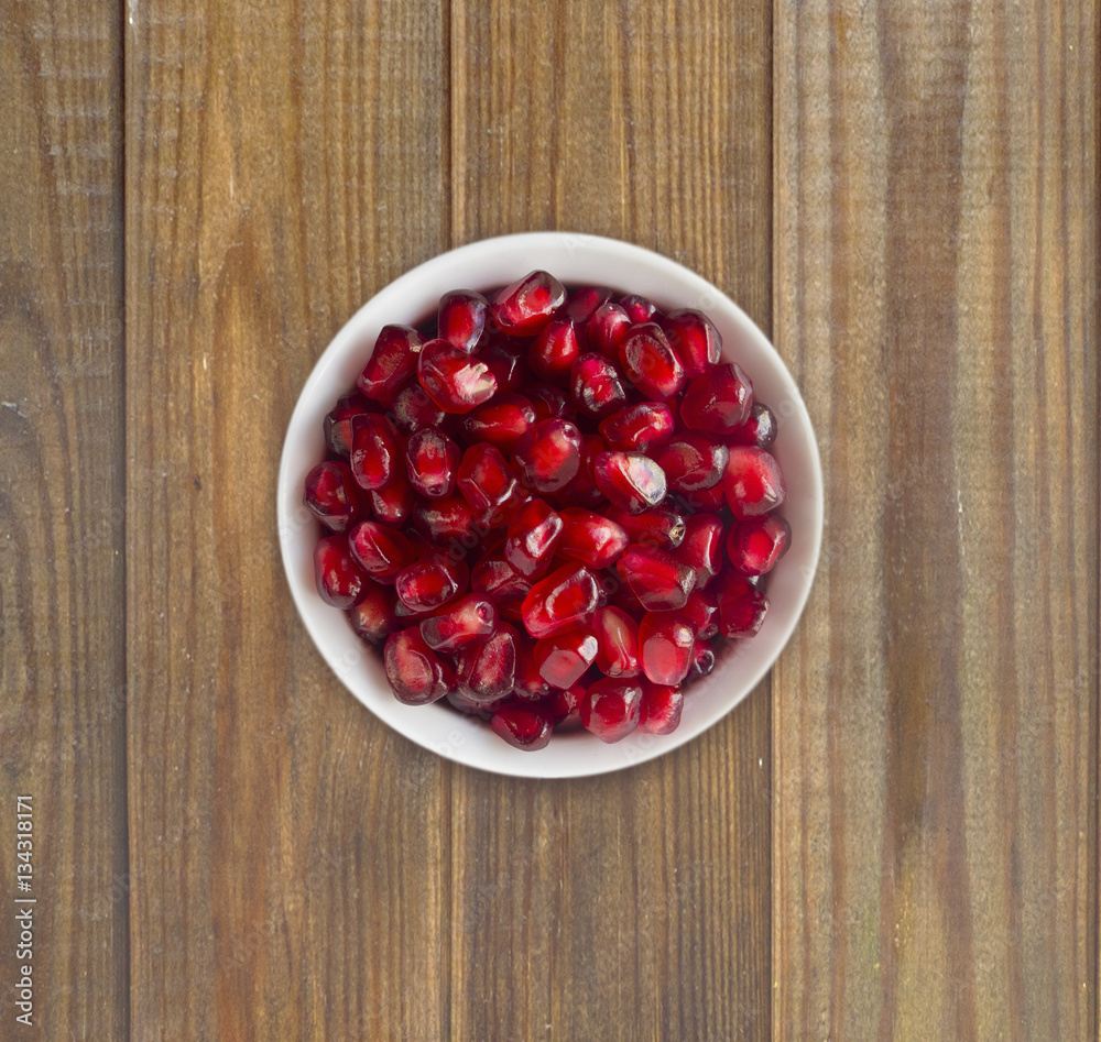 Pomegranate seeds on a wooden background. Red grains of a pomegranate in ceramic bowl. Top view. Pomegranate seeds on a wooden background. Red grains of a pomegranate in ceramic bowl. Top view.