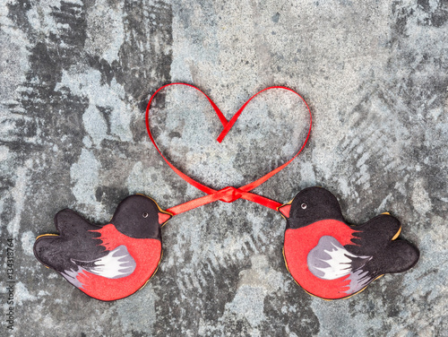 Gingerbread cookie shape of birds bullfinches hearts red ribbon love valentine day concept. Sweet cookies bullfinches on a gray grunge background