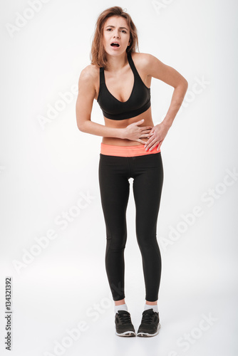 Sad young fitness lady with painful holding belly