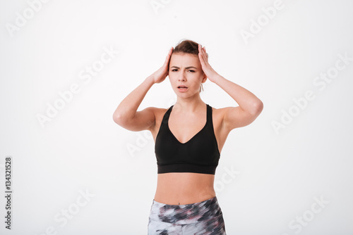 Confused young fitness lady holding head with hands