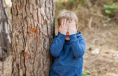 Fotografía Little Caucasian boy closing his face with hands as if playing hide and seek or scared of something