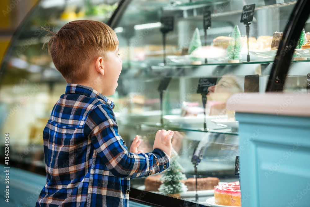 Back view of little boy choosing cake in showcase