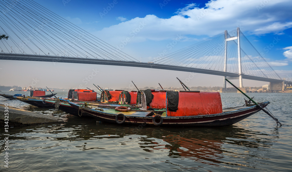 Wooden boats lined up at the Hooghly river bank overlooking the famous Vidyasagar setu bridge. Wooden boats lined up at the Hooghly river bank overlooking the famous Vidyasagar setu bridge.