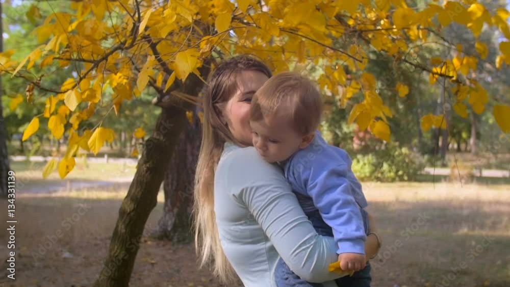Slow motion steadicam shot of beautiful smiling mother cuddling her baby under tree at autumn park Slow motion steadicam shot of beautiful smiling mother cuddling her baby under tree at autumn park