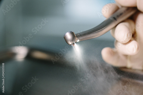 Doctor holding a dental drill tool atomizes spray the water and air by hand with protective gloves. background: work in clinic (operation, tooth).