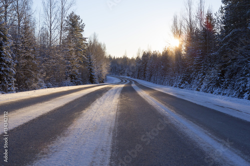 Empty asphalt road on a winter morning. Sun is about to rise behind the forest. Image has flare effect added. © Jne Valokuvaus