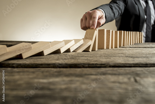 Hand of businessman stopping falling domino pieces