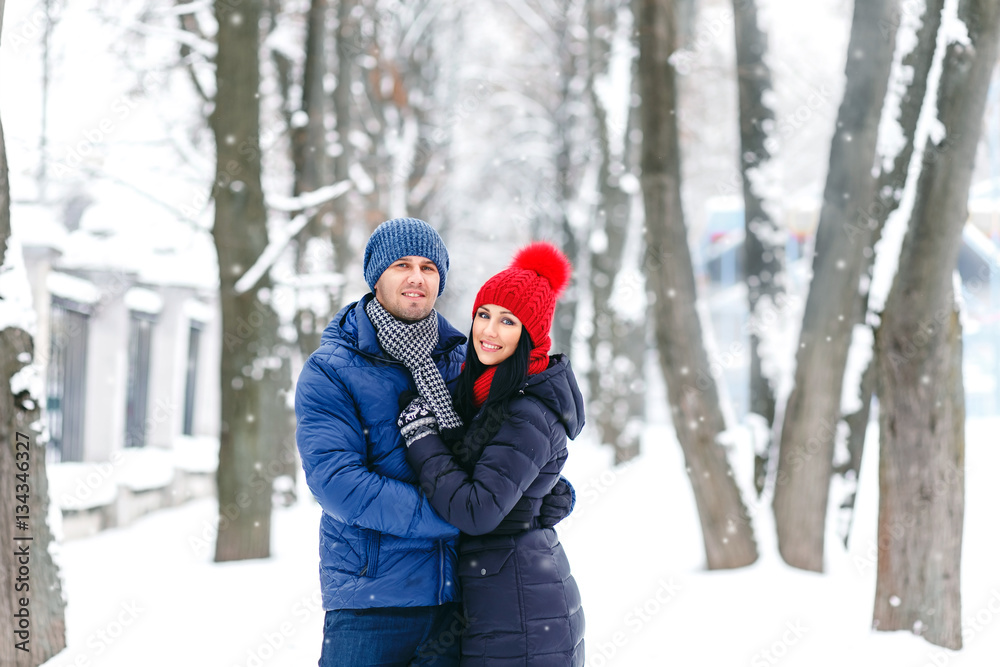 portrait of pretty young happy couple in love walking and playing in winter park in red hat and pullover. happy family Valentine's Day together. portrait of pretty young happy couple in love walking and playing in winter park in red hat and pullover. happy family Valentine's Day together.