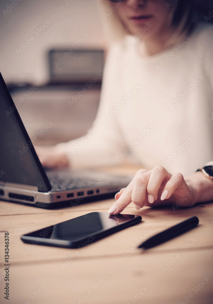 Closeup view of female finger touching black screen modern smartphone on the wooden table.Concept young business people using mobile devices at workplace.Vertical, blurred background. Closeup view of female finger touching black screen modern smartphone on the wooden table.Concept young business people using mobile devices at workplace.Vertical, blurred background.