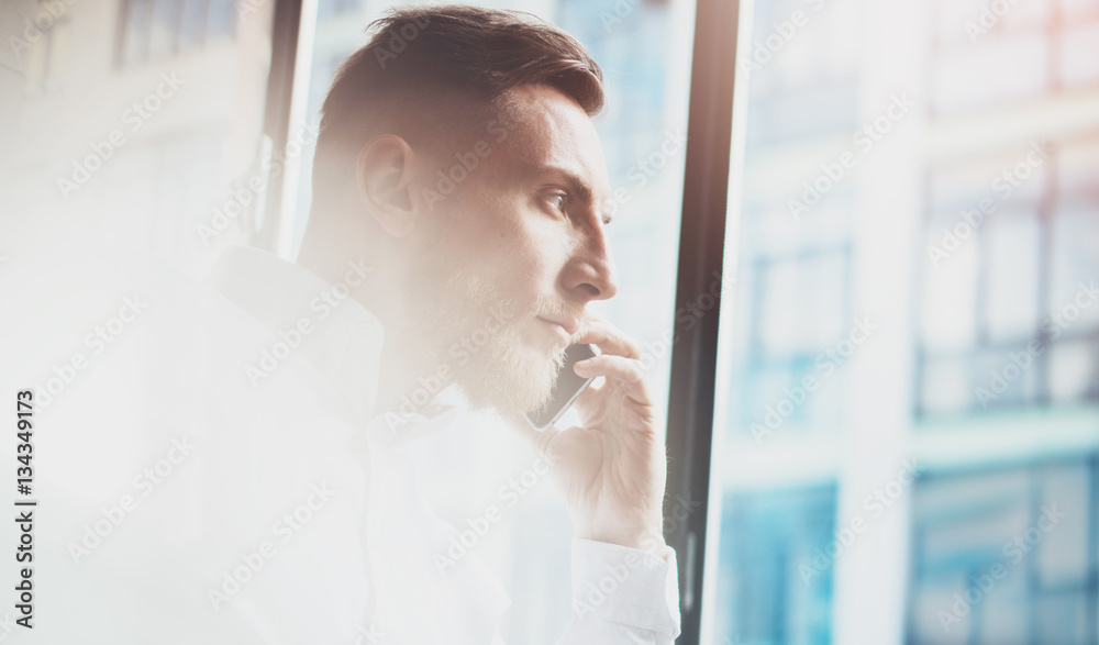Portrait of bearded man making mobile call at working place.Guy sitting in chair and looking out the panoramic window.Skyscraper office building blurred on background.Horizontal. Portrait of bearded man making mobile call at working place.Guy sitting in chair and looking out the panoramic window.Skyscraper office building blurred on background.Horizontal.