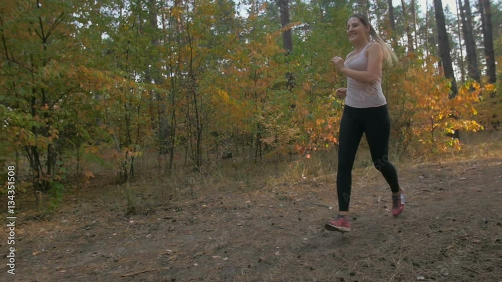 Slow motion of beautiful smiling young woman jogging in forest at evening Slow motion of beautiful smiling young woman jogging in forest at evening