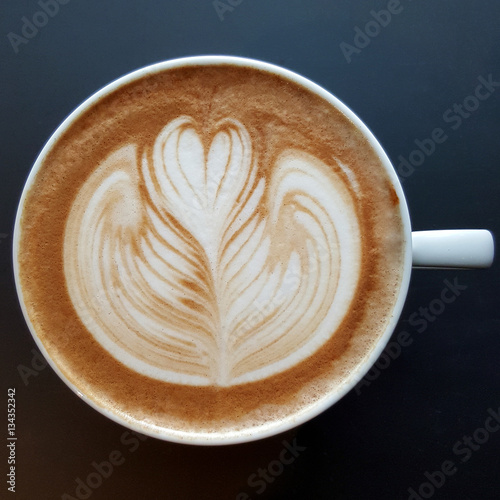 Top view of a mug of latte art coffee on black background.