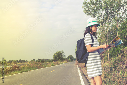 young asian woman with backpack standing on side road and readin