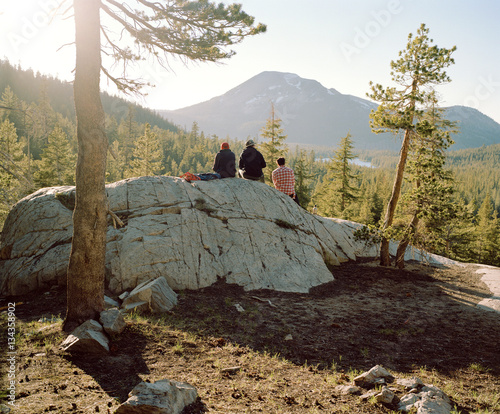 People sitting on large rock in forest with mountains