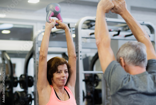 Senior couple in gym working out using kettlebells. photo