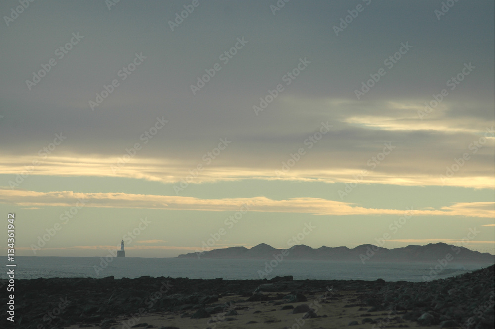 Silhouetted lighthouse and sand dunes at dusk, Scotland.