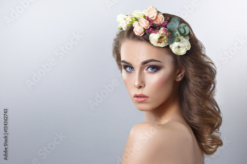 Delicate spring beauty portrait of a beautiful girl with a wreath of flowers on his head isolated on a gray background. © ksi