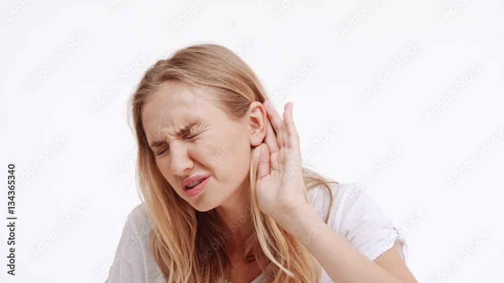 Young beautiful Caucasian blonde girl trying to hear something showing ear on white background in slowmotion