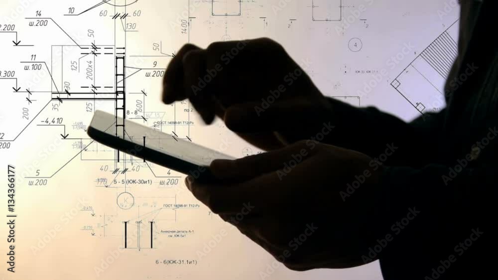 Silhouette of hands using Tablet PC while working with Blueprints.