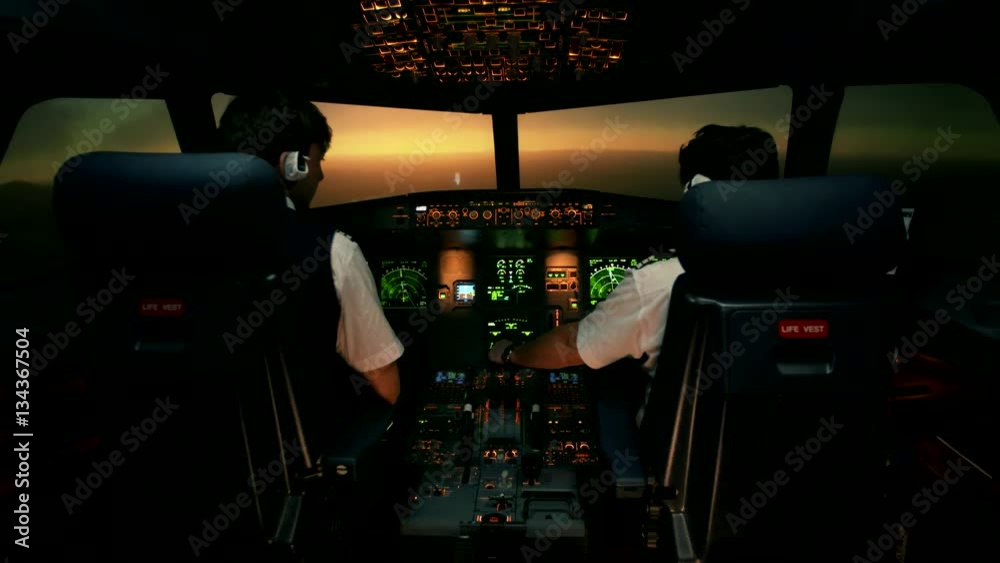 Modern passenger aircraft during descent. Sunset view from the cabin of modern plane to the Airport ruway with lighting. Two professional male pilots in the cockpit or flight deck control airplane