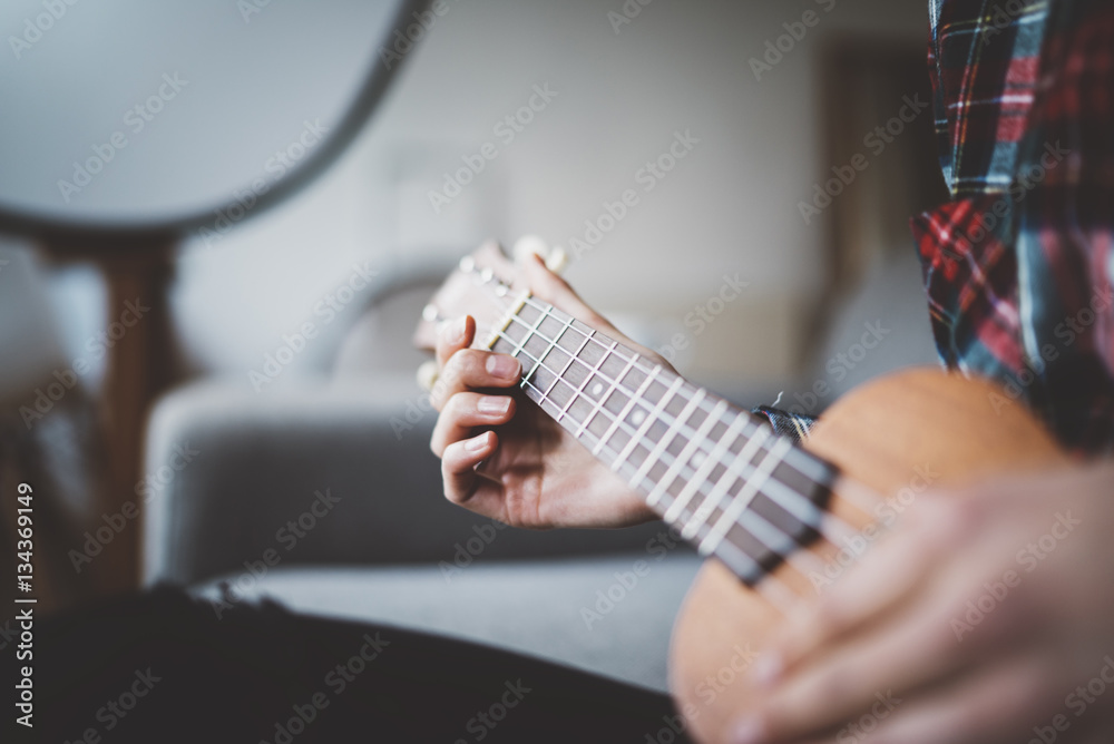 Close-up of female hands olaying ukulele guitar at cozy home interior, enjoyment concept