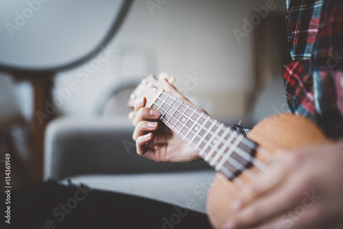 Close-up of female hands olaying ukulele guitar at cozy home interior, enjoyment concept