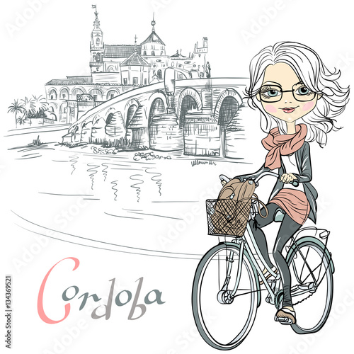 Cute beautiful fashionable girl rides a bike in Cordoba  Andalusia  Spain. Mosque Mezquita and Roman bridge on the background