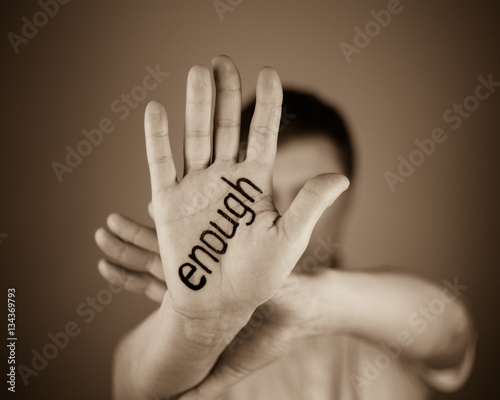 man showing  the word "enough" written on the palm of a his hand