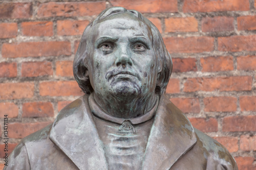 Bronze statue of the reformer Martin Luther in front of a brick wall