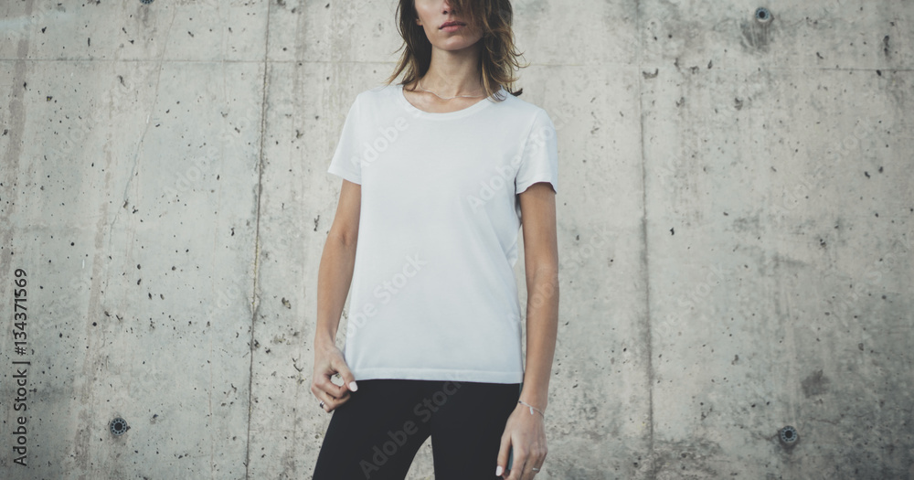 Naklejka premium Pretty young fit girl wearing blank white t-shirt with copy space for your logo or design, mock-up of template t-shirt, concrete grey wall in the background
