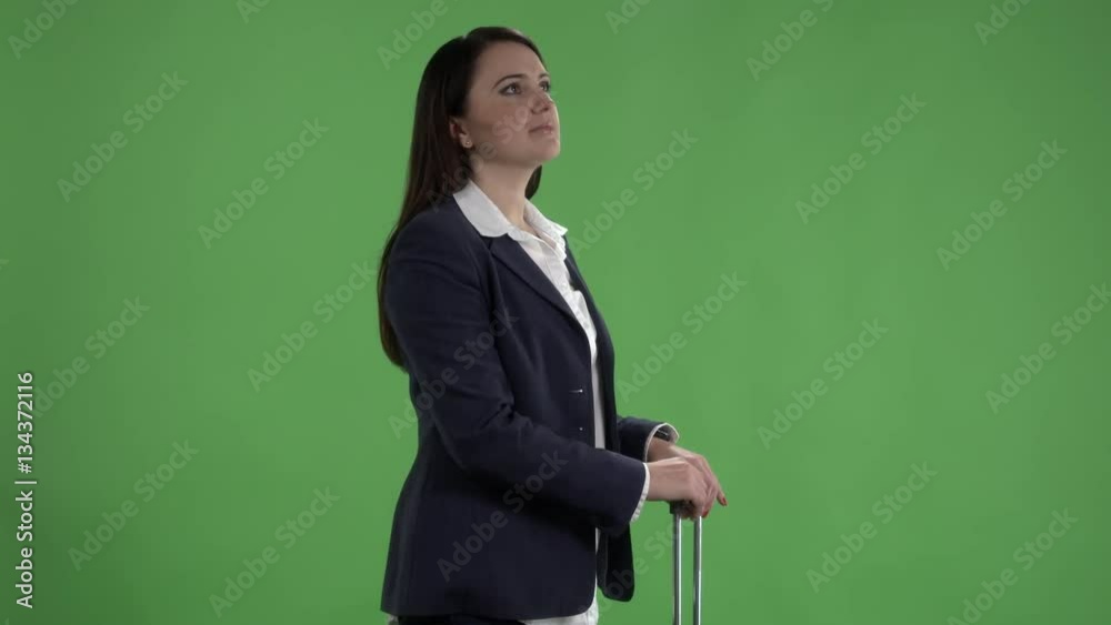 Woman with suitcase looking at watch and checking schedule on departure board against green screen